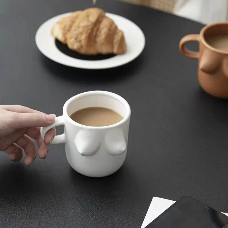 Person holding a white mug with coffee on a dark surface with a croissant in the background.