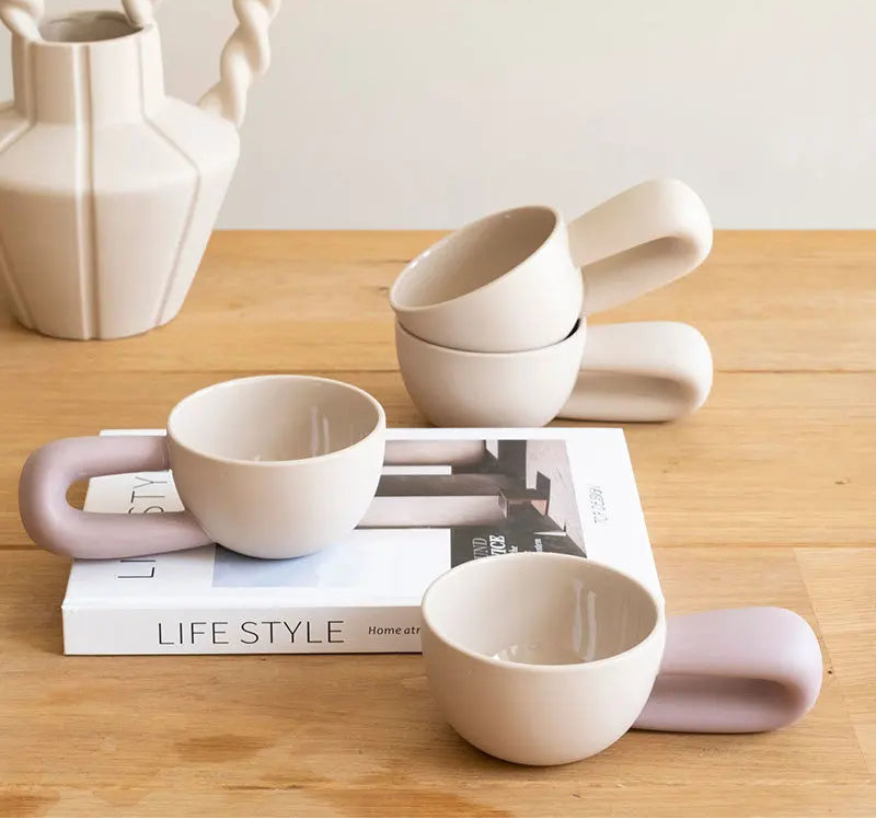 Set of ceramic cups with handles on a wooden surface with a magazine underneath.