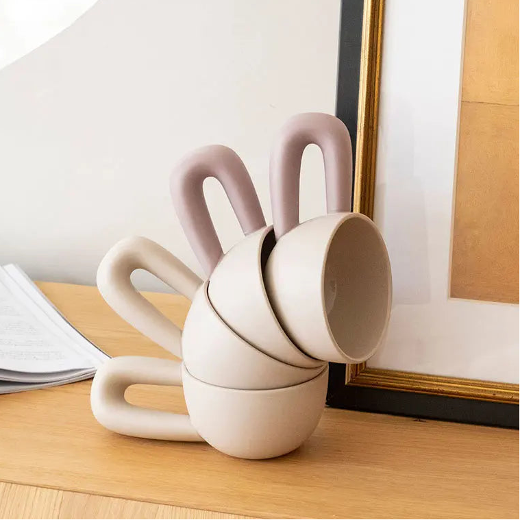 Stack of unique ceramic cups on a wooden surface with a mirror in the background.