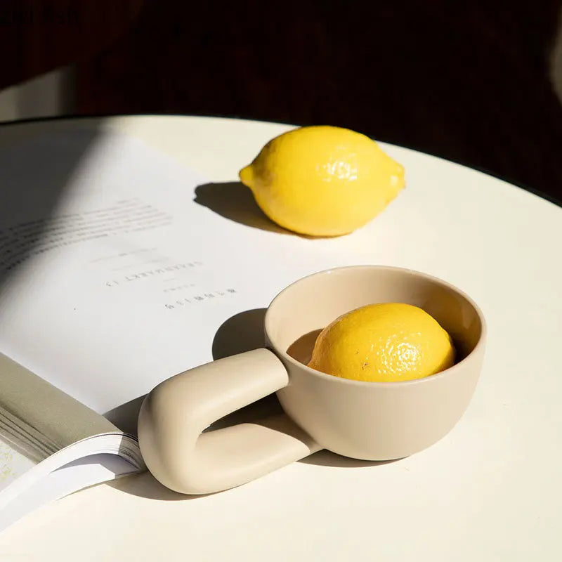 Two lemons on an open book with a beige ceramic cup.