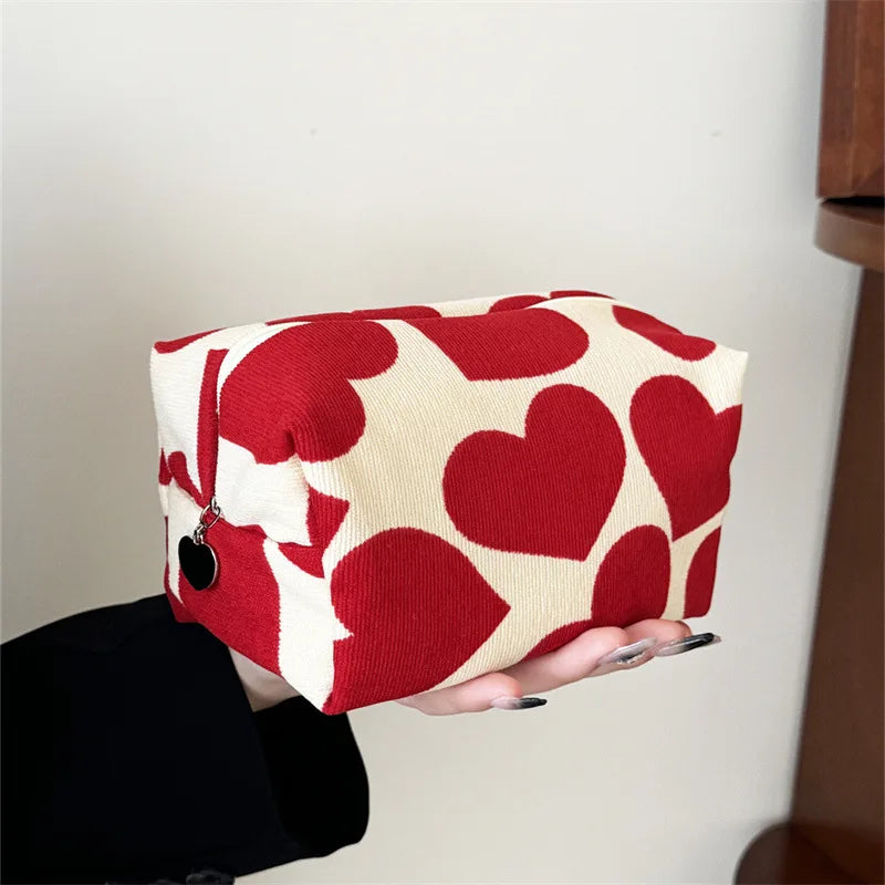 Red and white heart-patterned pouch held by a person against a neutral background