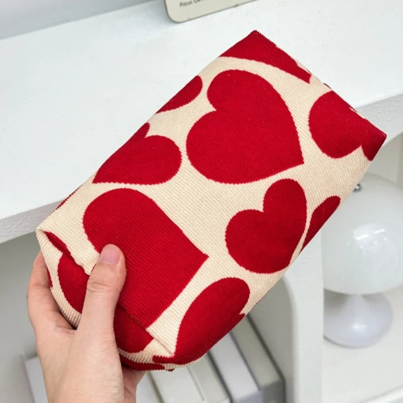 Red heart-patterned pouch held by a hand on a white surface